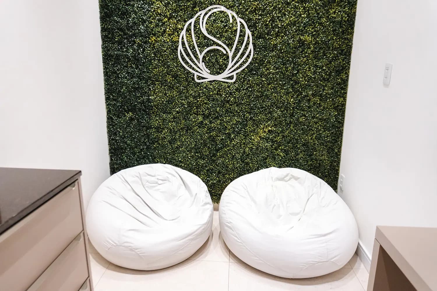 Espaço acolhedor com pufes e parede verde com o símbolo Sommus, ótimo para atendimento infantil